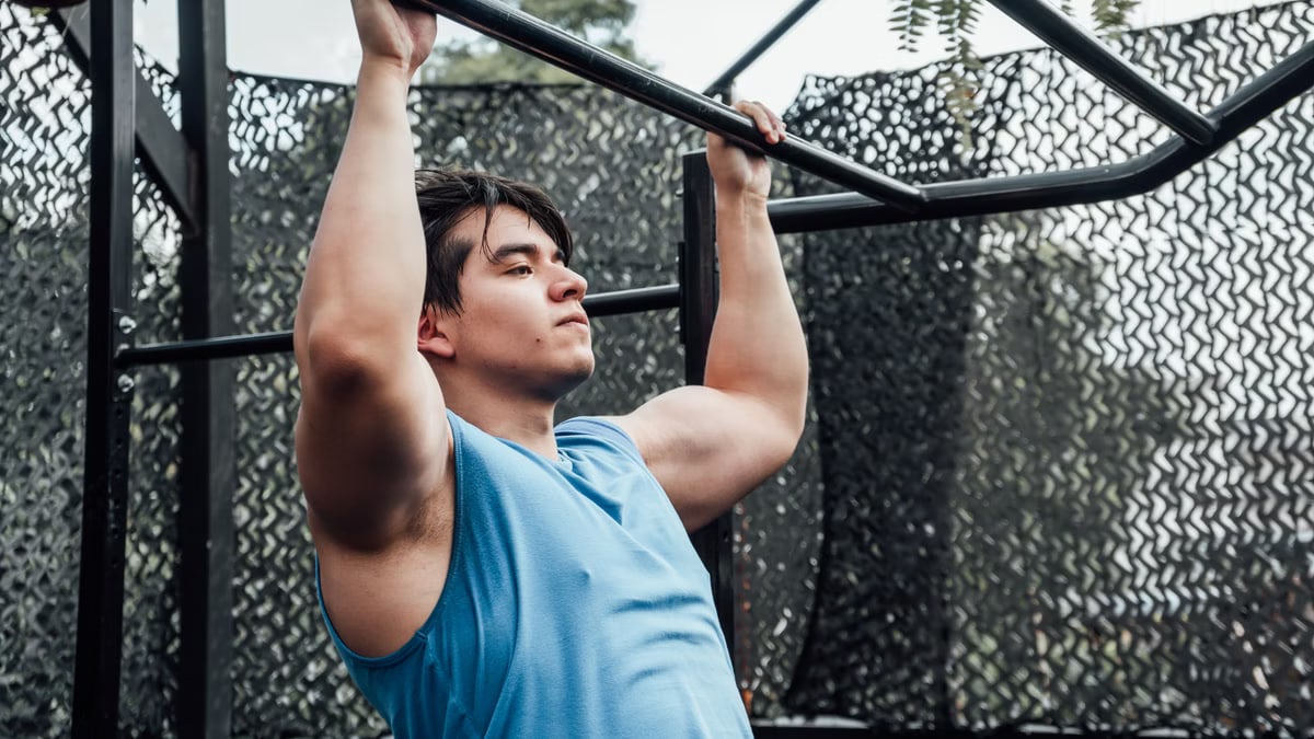 Muscular man in blue tank top performing pull-ups outdoors in Mexico City.